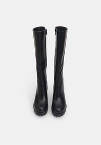 Botas negras de cuero hasta la rodilla con acabado liso, punteras redondas y cremalleras laterales. Suelas gruesas de goma para mayor agarre y durabilidad.