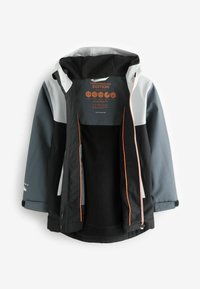 Vandtæt jakke i sort, grå og hvid med en orange lynlås. Har hætte, blød inderforing og et Performance Edition mærke indeni.