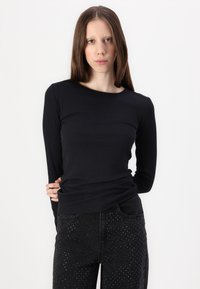 Musta pitkähihaine paita, jossa on ribbitoitu pinta ja pyöreä kaula-aukko, yhdistetty mustiin farkkuihin, joissa on pistekuvioita ja taskut.