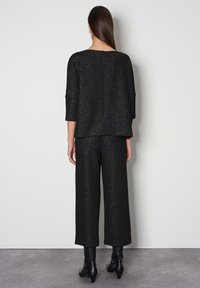 Schwarzes Outfit mit separates, bestehend aus einer lockeren Bluse mit Dreiviertelärmeln und weit geschnittenen Hosen, beide mit einem subtilen Schimmer-Effekt.
