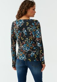 Zwarte longsleeve met een kleurrijke bloemenprint in blauw, roze en goud. Zachte stof met een getailleerd ontwerp, ronde halslijn en aansluitende mouwen.