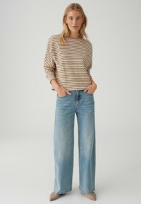 Maglione a righe beige e crema abbinato a jeans azzurri a gamba larga. Tessuto morbido con vestibilità casual, accenti minimali e scollo arrotondato.
