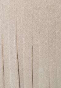 Faltiger beiger Stoff mit strukturierten Oberflächen. Verfügt über vertikale Linien, die ein Muster bilden, und ist aus einem weichen, leichten Material gefertigt.