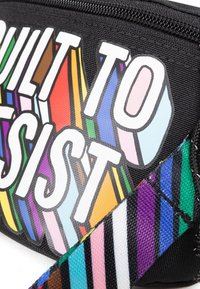 Mustassa kankaisessa laukussa on värikäs teksti "BUILT TO RESIST." Erityiset yksityiskohdat sisältävät monivärisen raidallisen olkahihnan ja teksturoitu pinnan.