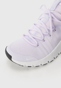 Baskets de course Nike en tissu lavande clair. Comprend des lacets ronds, des œillets renforcés, et une semelle en caoutchouc texturé noir avec des accents blancs.