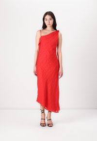 Raudona asimetriška suknelė su įstrižais raštais, pasižyminti tekstūruota medžiaga ir plonomis petnešėlėmis. Dėvima su juodais sandalais su kabliukais.