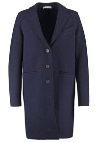 Tummansininen villakangastakki, jossa on lovettu kaulukset, pitkät hihat, neljä etunappia ja kaksi sivutaskua. Pehmeä, teksturoitu kangas ja räätälöity malli.