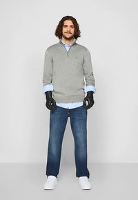 Siv pulover z zadrgo preko svetlo modre srajce z ovratnikom, kombiniran z modrimi kavbojkami in belimi supergami. Črne rokavice zaključujejo obleko.