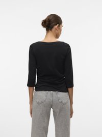 Svart langermet topp med båthals, glatt tekstur, kombinert med lysegrå høy midje jeans med et klassisk fem-lommers design.