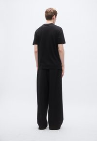 Fekete, rövid ujjú pamut póló klasszikus kerek nyakkal, laza szabású fekete nadrággal párosítva. Matt textúra, minimalista design.