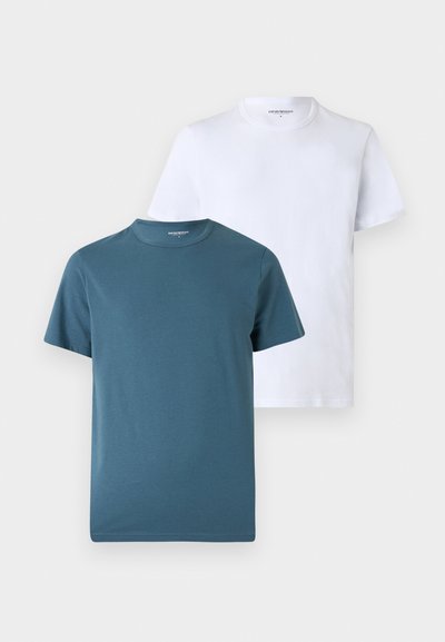 Δύο μονόχρωμα μπλουζάκια με κοντό μανίκι και στρογγυλή λαιμόκοψη, ένα σκούρο τιρκουάζ μπροστά και ένα λευκό πίσω, απεικονίζονται σε ανοιχτό φόντο.