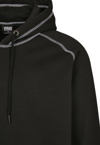 Crna majica s kapuljačom na vezanje, s kontrastnim bijelim šavovima na šavovima. Mekana tkanina s rebrastim teksturama na manžetama.