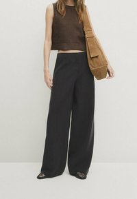 Débardeur marron court, pantalons larges noirs et sac à bandoulière en daim marron. Comprend une coupe ample et des chaussures ouvertes à motifs découpés.