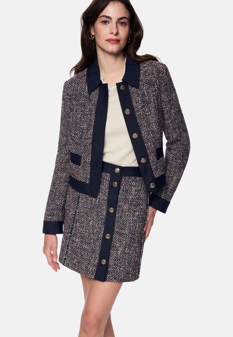 Tweed jacket and skirt set in navy, red, and cream. Features a collar, gold buttons, and side pockets on the jacket. Structured silhouette.