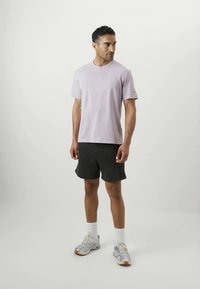 Lys lilla kortærmet t-shirt med rund halsudskæring, parret med mørke shorts. Model bærer hvide sokker og atletiske sko med sølvdetaljer.