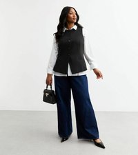 Gilet noir cintré avec des boutons, chemise blanche à col en dessous, jean noir à jambes larges, et un petit sac à main noir. Talons noirs brillants.