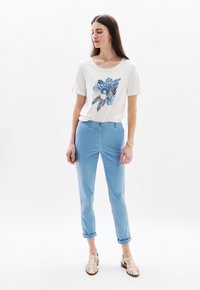Witte katoen t-shirt met blauwe bloemenborduurwerk, gecombineerd met lichtblauwe broeken en beige sandalen met bandjes. Vlotte textuur, casual pasvorm.