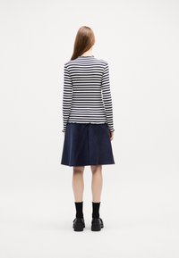 Schwarz-weiß gestreiftes Langarmoberteil kombiniert mit einem marineblauen Cordrock, ergänzt durch schwarze Schuhe und kniehohe Socken.