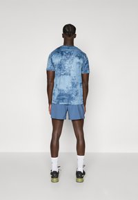 T-shirt de sport bleu avec un motif texturé, accompagné de shorts assortis. La tenue présente des manches courtes et des chaussures de sport.
