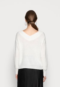 Weißer gestrickter Pullover mit V-Ausschnitt hinten, überschnittenen Schultern und lockerem Schnitt, kombiniert mit einem schwarzen Faltenrock.