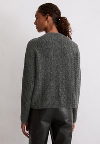 Grauer Strickpullover mit strukturiertem Rippmuster, überschnittenen Schultern und lockerer Passform, kombiniert mit schwarzen Lederhosen.