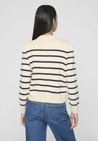 Krēmas krāsas džemperis ar tumši ziliem horizontāliem svītrām. Iezīmēta apaļa apkakle un ribota aproces, apvienots ar ziliem džinsiem. Mīksta adīšanas tekstūra.