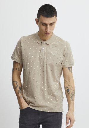 Beige polo t-shirt med et tekstureret mønster af små diamanter, krave med to knapper, korte ærmer og broderet logo på brystet.