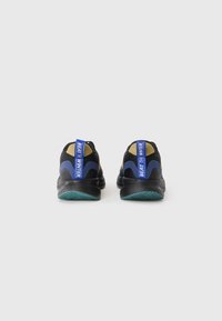 Baskets de sport noires avec des accents bleus et dorés, présentant une surface texturée et une languette au talon bleue "BATTRE L'HIVER". Semelle en caoutchouc.