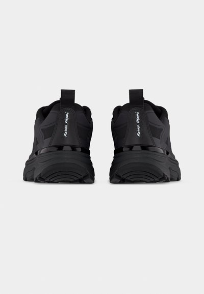 Paire de baskets de sport noires avec semelles épaisses, languettes de traction au talon visibles et branding en script blanc à l'arrière sur fond uni.