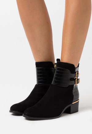 Černé kotníkové boty s nubukovým svrškem a kůží s kroko vzorem na manžetě, zlaté přezky jako akcenty a skromný blokový podpatek.