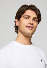 Witte ronde hals t-shirt van katoen, voorzien van een klein zwart logo op de linkerborst. Soepele textuur met korte mouwen.