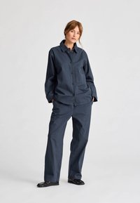 Námornícky modrý bavlnený outfit so zapínaním na gombíky, ktorý zahŕňa košeľu s vreckom na hrudi a pohodlné nohavice s širokými nohavicami. Hladká textúra, ležérny dizajn, minimálne detaily.
