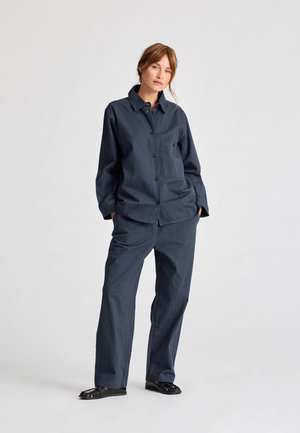 Navy blue cotton outfit featuring a button-up shirt with a chest pocket and wide-leg trousers. Smooth texture, casual design, minimal accents.
