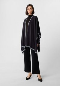 Ciemny poncho z kontrastowym, jasnoszarym wykończeniem, o miękkiej teksturze i płynnej linii. Połączone z czarnymi spodniami o szerokich nogawkach i czarnymi szpilkami.