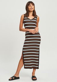 Schwarz-weiß-orange gestreiftes Maxikleid mit tailliertem Design, geripptem Material und seitlichem Schlitz. Tragen mit schwarzen Riemchensandalen.
