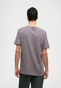 Lilla bomulds t-shirt med korte ærmer og rund halsudskæring, vist fra ryggen. Glat tekstur, afslappet pasform, ingen synlige mønstre.