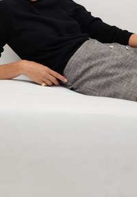 Pull en maille noir associé à une jupe à carreaux grise avec des détails de boutons. La jupe a une texture douce et une silhouette structurée.