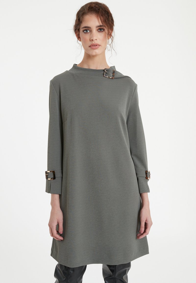 Gray garment with a high neckline and a side buckle detail. Long sleeves with buckle accents at cuffs, made from a smooth, textured fabric.