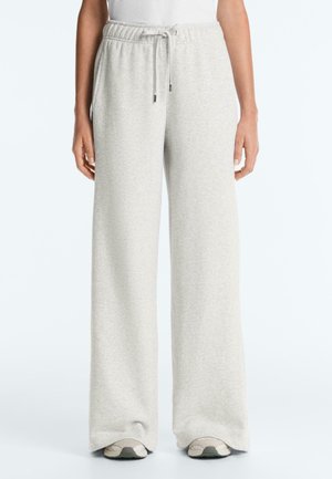 Osoba nosi svetlosivé široké teplákové nohavice s elastickým pásom a šnúrkou, v kombinácii s bielymi teniskami.