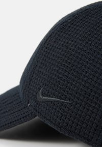 Czarna, teksturowana czapka z zakrzywionym daszkiem, posiada subtelnie wytłoczone logo Nike. Materiał wydaje się oddychający i pleciony.