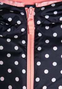 Giacca puffer blu navy con pois bianchi, dotata di zip e rifiniture rosa. Il tessuto è liscio e leggermente lucido.