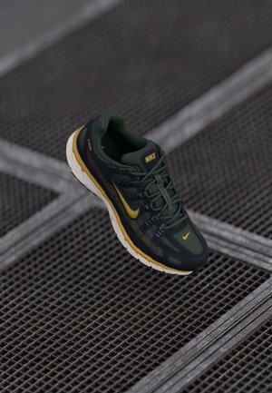 Pantofi de alergare Nike în verde închis cu accente galbene, realizati din material textil și sintetic, talpă texturată și sistem de șireturi.