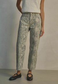 Ljust gröna jeans med ormtryck och hög midja, med rak benprofil, framfickor och knappstängning. Åtföljs av svarta lägenheter.