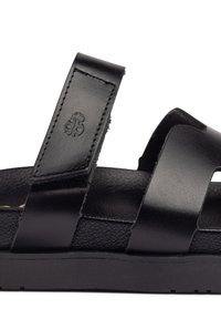 Sandale en cuir noir avec un dessus texturé, dotée de larges sangles et d'une semelle robuste en caoutchouc noir. Comprend un détail de logo en relief sur la sangle.