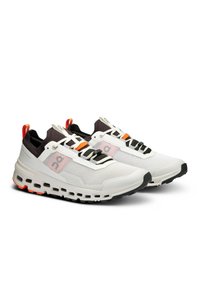 Baskets de sport blanches avec une tige en mesh, des accents noirs, des détails orange et une épaisse semelle perforée. Dispose d'un système de laçage unique et de poignées.