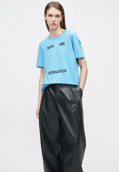 Ανοιχτό μπλε βαμβακερό t-shirt με μαύρο κείμενο: «BAUM UND PFERDGARTEN.» Συνδυασμένο με ψηλόμεσα, μαύρα, δερμάτινα παντελόνια με φαρδιά πόδια.