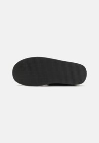 Semelle de chaussure en caoutchouc noir avec un motif texturé et des bords arrondis, présentant une surface lisse et une épaisseur constante.