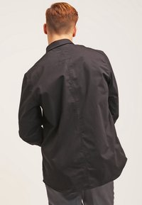 Maglietta nera a maniche lunghe con una texture liscia, colletto strutturato e dettaglio del giromanica sul retro. Design semplice con una vestibilità rilassata e orlo dritto.