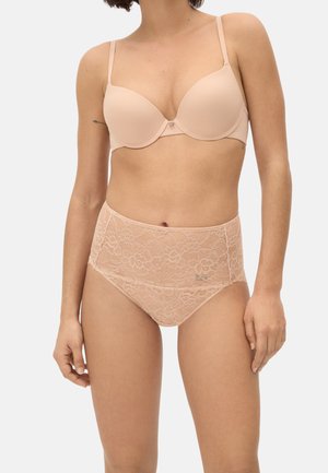 Mujer con un sujetador acolchado color nude de tirantes delgados y ropa interior de encaje floral de talle alto contra un fondo claro y sencillo.