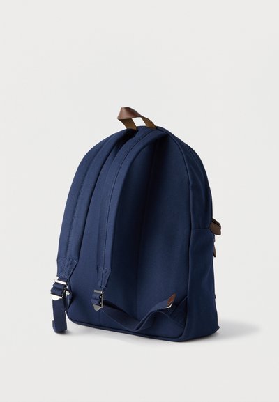 Σακίδιο πλάτης σε ναυτικό μπλε με δύο ρυθμιζόμενους επενδυμένους ιμάντες και καφέ δερμάτινη χειρολαβή με βρόχο σε απλό λευκό φόντο.